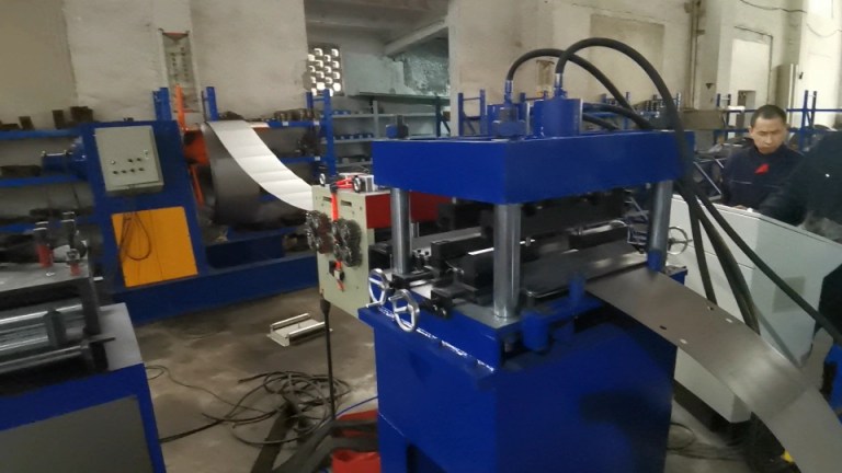 An industrial setting showing a hydraulic uncoiler with a large steel coil, connected to a yellow servo feeder mechanism, preparing the steel for further processing.