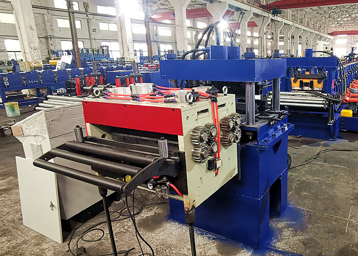 A servo feeder guiding a flat steel sheet into a large, blue industrial punching device with multiple hydraulic cylinders, located within a factory.
