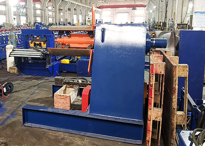 A large hydraulic uncoiler holding a massive coil of galvanized steel, positioned in a spacious industrial workshop.