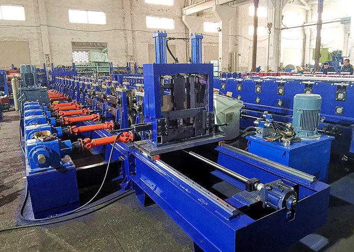 A complete view of a blue and yellow C/Z purlin roll former machine, stretching across a clean factory floor with a large coil of steel at the input and multiple roll forming stations.
